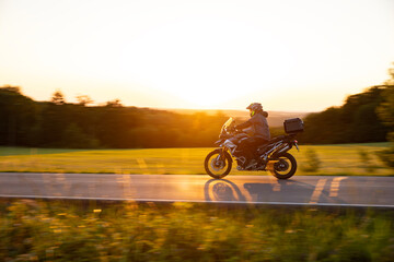 Driver riding motorcycle on empty road during sunset, spring mountains