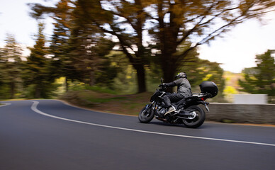 Driver riding motorcycle on empty asphalt road, spring mountains