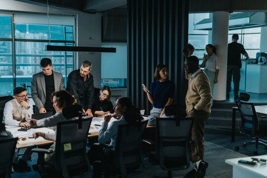 A diverse and multigenerational team of business people engaged in a lively brainstorming session, fostering teamwork and creative thinking in a contemporary office environment. - Powered by Adobe
