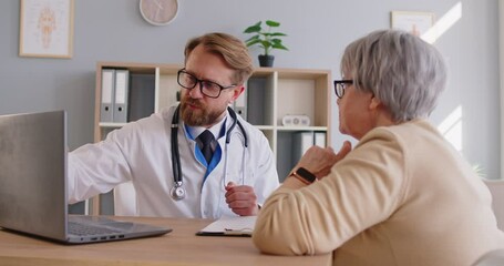 Experienced male doctor explaining lab tests results to senior woman who came on medical appointment, giving prescription and recommendations. Old patient being on check up in clinic - Powered by Adobe
