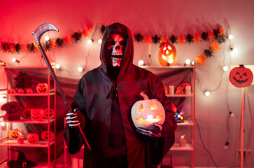 Portrait of male person in grim reaper death costume in black cloak with hood looking at camera...