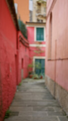 Obraz premium Blurred view of colorful alley with red walls and windows, capturing an urban outdoor scene with soft bokeh effect suggesting an italian setting.