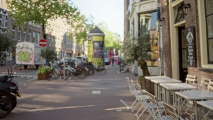Blurred european city street scene featuring bicycles, outdoor tables, graffiti, and trees, capturing the essence of urban life with a defocused background suggesting a bustling atmosphere.