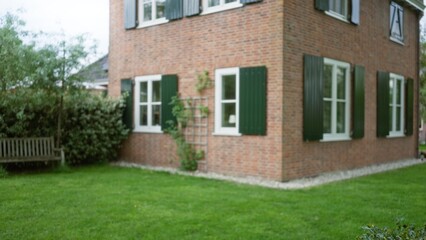 Blurred view highlighting a serene and picturesque house with red brick, green shutters, and lush garden, captured in defocused style emphasizing tranquility and real estate appeal.