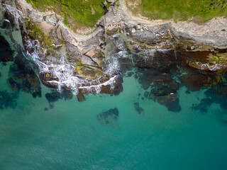 Aerial top-down view of turquoise sea waves crashing over rocky coastline with moss and clear water. Wild nature texture along the Bulgarian coast, dramatic and scenic