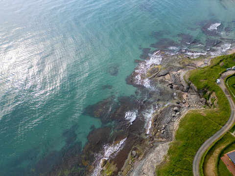 Aerial top-down view of turquoise sea waves crashing over rocky coastline with moss and clear water. Wild nature texture along the Bulgarian coast, dramatic and scenic