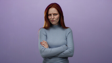 Obraz premium Woman with red hair stands arms crossed against purple background in thoughtful pose, showcasing serene expression in soft lighting, wearing blue sweater and conveying tranquility