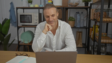 Middle-aged caucasian man with blonde hair in white shirt working on laptop in modern office...