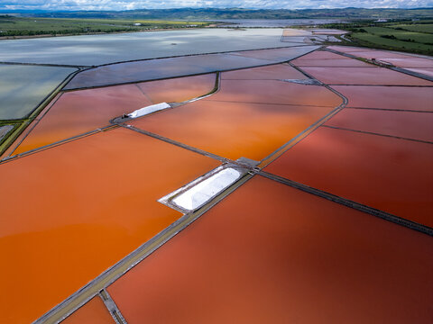 Aerial view of colorful salt pans near Burgas, Bulgaria. Vibrant red and orange evaporation ponds contrast with white salt piles and turquoise sea. Industrial and natural beauty combined