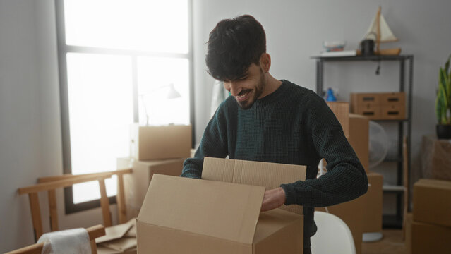 Young man unpacking boxes in a new home, surrounded by furniture and natural light in a cozy apartment setting.