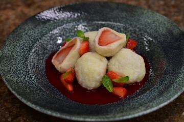 Fruit dumpling with strawberry sauce served on a blue plate – traditional sweet dish with vibrant colors and soft texture.