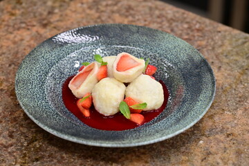 Fruit dumpling with strawberry sauce served on a blue plate – traditional sweet dish with vibrant colors and soft texture.