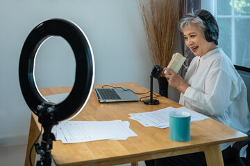 Senior influencer Asian woman unboxing gift box in live streaming with professional setup