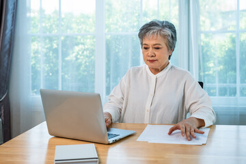Senior Asian businesswoman manager working on laptop at office desk with documents in professional environment
