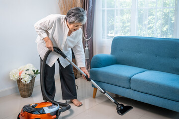 Senior Asian woman cleaning floor with vacuum cleaner at home