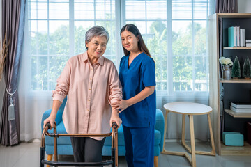 Senior Asian woman using walker with supportive female caregiver nurse in home environment, looking at camera
