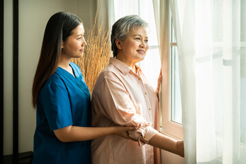 Senior Asian woman smiling with female caregiver nurse by window in home care