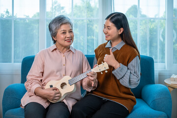 Asian elderly woman practicing ukulele with granddaughter encouragement