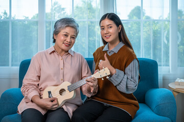 Senior Asian elderly woman learning ukulele with granddaughter support and encouragement, looking at camera