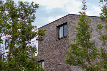 A fragment of a building with a brick façade of raw, industrial character, featuring a window. In the background, a blue sky and lush green trees – the building set against the sky and greenery.