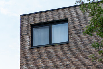 brick wall with window,A fragment of a building with a brick façade of raw, industrial character, featuring a window. In the background, a blue sky and lush green trees – the building 
