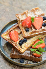 Bright and airy breakfast scene featuring waffles topped with fresh strawberries, blueberries, and mint leaves, beautifully plated.