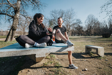 Two young teenagers enjoy each other's company while resting on a bench in a sunny urban park,...