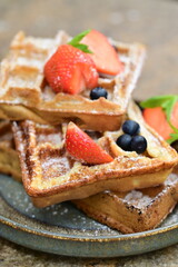 Bright and airy breakfast scene featuring waffles topped with fresh strawberries, blueberries, and mint leaves, beautifully plated.
