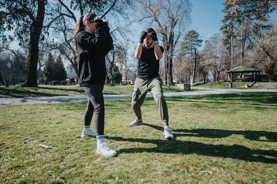 A young man and woman engage in an outdoor boxing training session in a park, emphasizing fitness and collaboration.