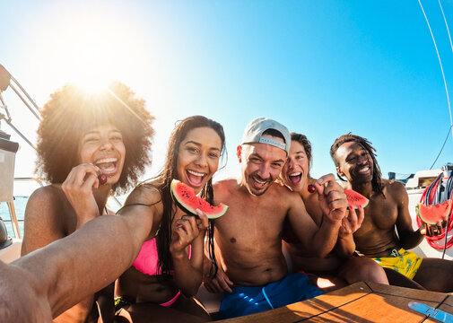 Happy multiracial friends eating watermelon while doing selfie duirng sea tour with sailing boat - Summer and vacation concept - Main focus on center man face