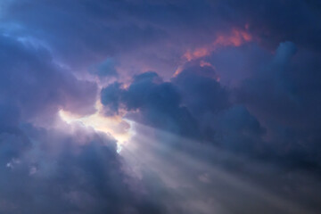 Sun rays breaking through dramatic purple and blue storm clouds at sunset, creating a serene and mystical atmosphere in the sky