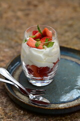 Close-up of Strawberries Romanoff dessert in a glass – layered fresh strawberries, whipped cream, and mint.