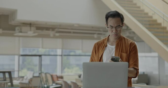 Senior Asian businessman wearing headset celebrates success during online meeting in modern co-working space. Remote work and business communication concept.	