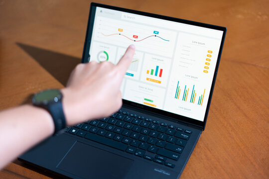 A person is pointing at a laptop screen with a graph on it