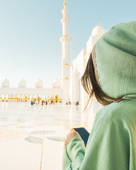 Sheikh Zayed Grand Mosque tour excursion or booking a visit concept.Female tourist visitor hold use phone post online travel photo check social media . Awe of iconic Islamic architecture in Abu Dhabi