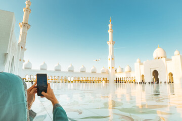 Tourist take photo of Luxury private jet landing above the iconic Sheikh Zayed Grand Mosque in Abu Dhabi. Modern aviation and Islamic architecture highlights opulence, travel, and cultural landmarks