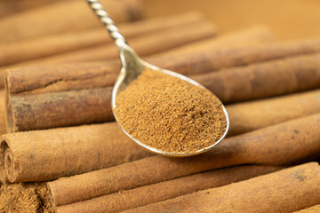 Ground cinnamon spice in a spoon and cinnamon sticks close-up