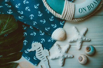Lifebuoy, starfish, seahorse, shells, green leaves and anchor printed on fabric on wooden white background. Summer seaside season