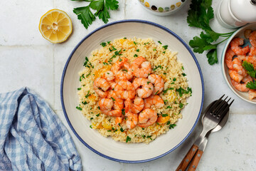 Mediterranean Couscous with fried Shrimps, yellow tomatoes, onion, parsley. White table surface. Top view.