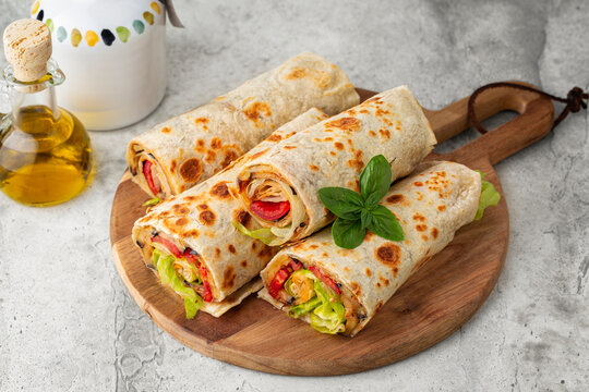 Piadina or tortilla on a wooden board. Wraps made with a soft flatbread rolled around a filling with vegetables and cheese, fried eggplant, tomato, lettuce. Vegetarian food concept.