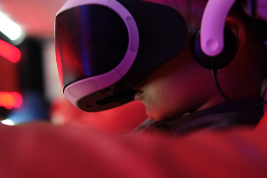 Fototapeta Child wearing VR Glasses. Surprised kid boy having fun play VR headset, virtual reality goggle, 3D cyber space. Futuristic neon blue red UV lighting. Digital technology, metaverse game, entertainment