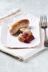 Grilled white sausage with ketchup on white paper tray. Rustic wooden background.