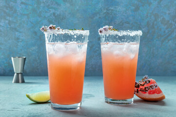 Salty Dog cocktail with fresh grapefruit juice, lime juice, and thyme, side view with a jigger and fresh fruit