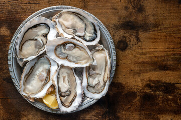 Fresh raw oysters on ice, overhead flat lay shot on a rustic wooden table, with lemon, with copy space