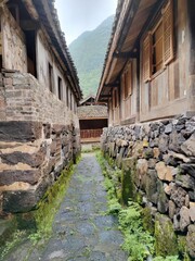 Moss-covered Stone Alley in Traditional Village &ndash; Perfect for Cultural Heritage, Historical Design, or Rural Aesthetic Projects. Showcases Rustic Architecture, Stone Paths, and a Mountainous Backdrop.