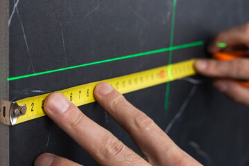 man measuring with tape with green laser level on wall