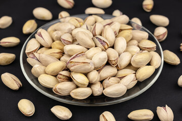 Heap of tasty pistachio nuts on the plate on dark background