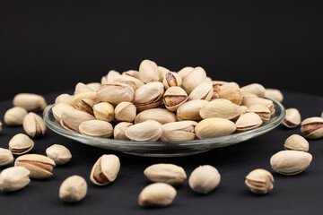 Heap of tasty pistachio nuts on the plate on dark background