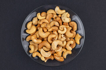 Top view of Roasted cashew nuts in glass bowl on dark background.