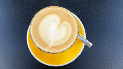 Cup of coffee with heart shape latte art on yellow saucer on dark cafe table
